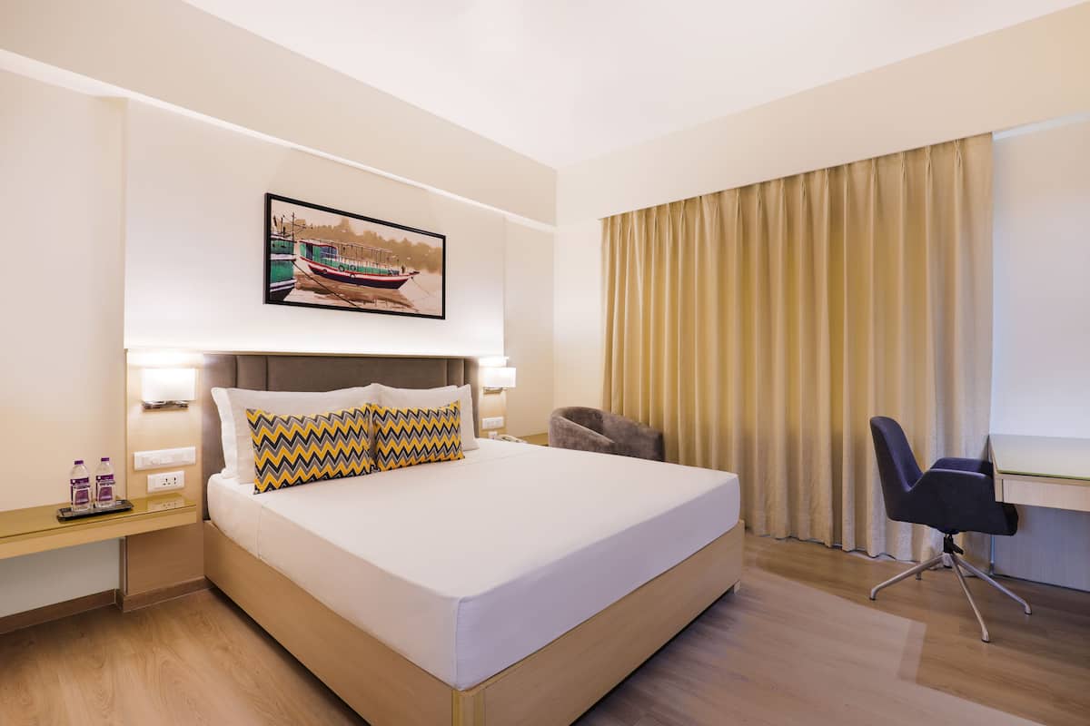 A hotel room with a large bed, a desk, a chair, and a window with curtains.