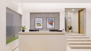 A reception area with a reception desk, framed artwork, a potted plant, and a staircase leading to another room. - Keys Lite Sreekanya Visakhapatnam (Visakhapatnam)