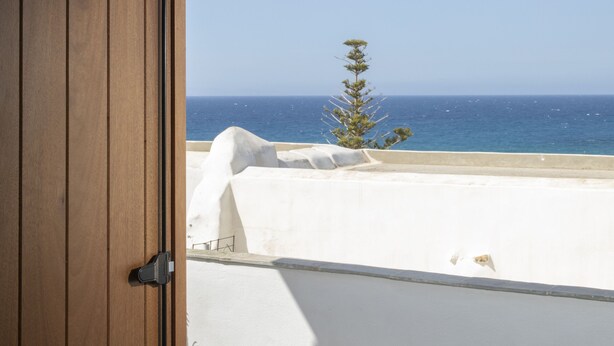 A wooden door leading to a balcony with a view of the sea and a small tree. - Cycladic sea view house (Naxos)