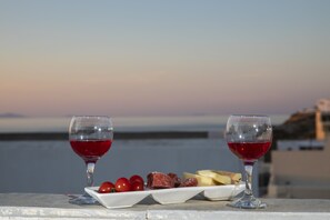 Zwei Gläser Rotwein und ein Teller mit Käse und Cocktailtomaten auf einem Balkon mit Blick aufs Meer.