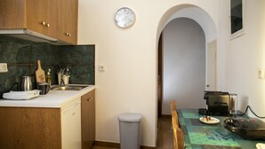 A kitchen with wooden cabinets, a sink, a clock, a trash bin, and a table with a coffee machine. - Cycladic sea view house (Naxos)
