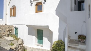 A white building with a stone staircase, a green door, and a small potted plant. - Cycladic sea view house (Naxos)