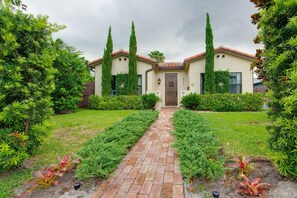 A house with a brick pathway leading to the front door, surrounded by well-maintained hedges and greenery.