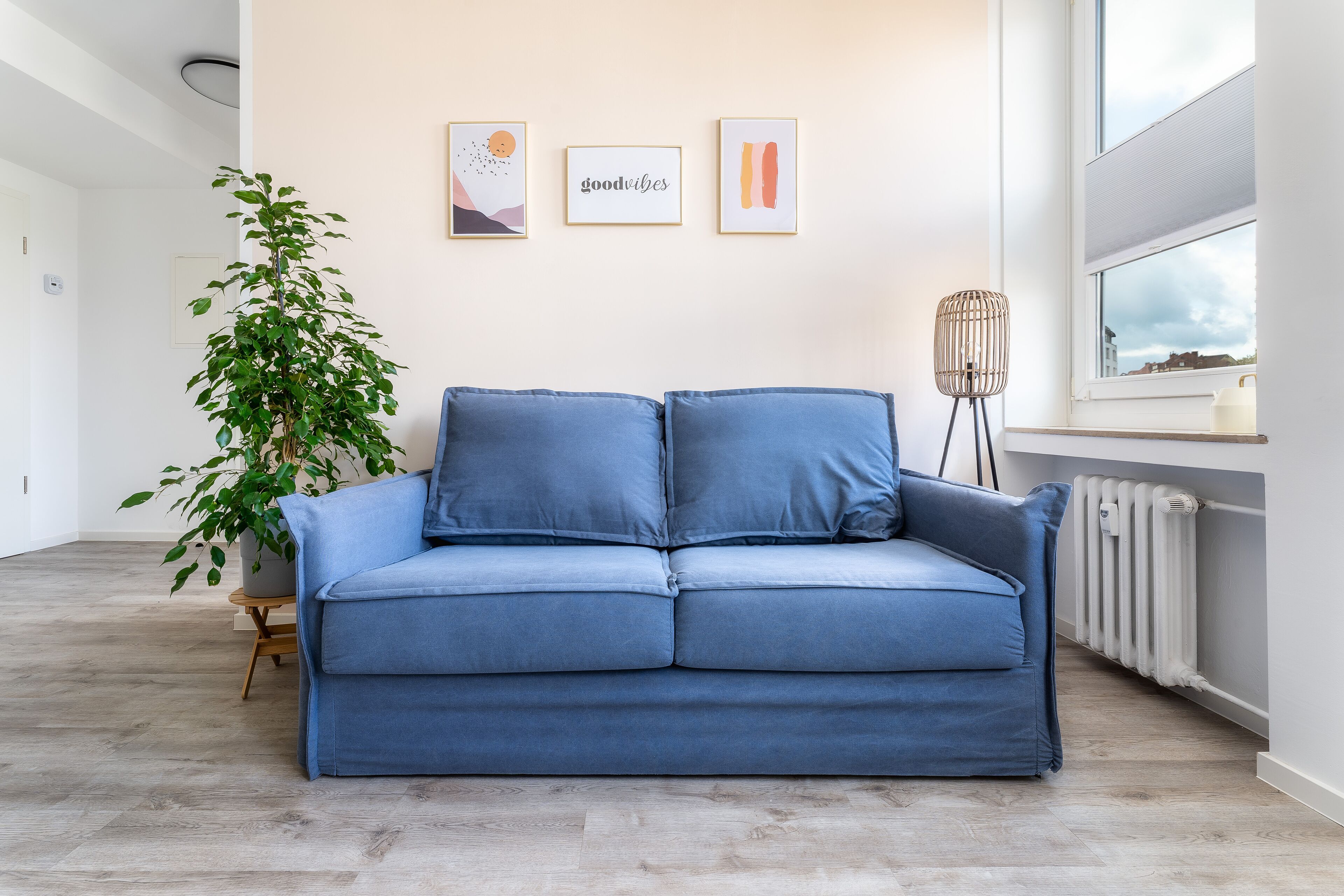 A modern living room with a blue sofa, a potted plant, and three framed artworks on the wall.
