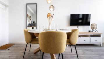 A modern dining area with a round table, four chairs, a flat-screen TV, and a white cabinet.