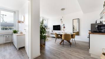 Una cocina moderna con comedor, armarios blancos y un amplio ventanal con vistas a un paisaje urbano.