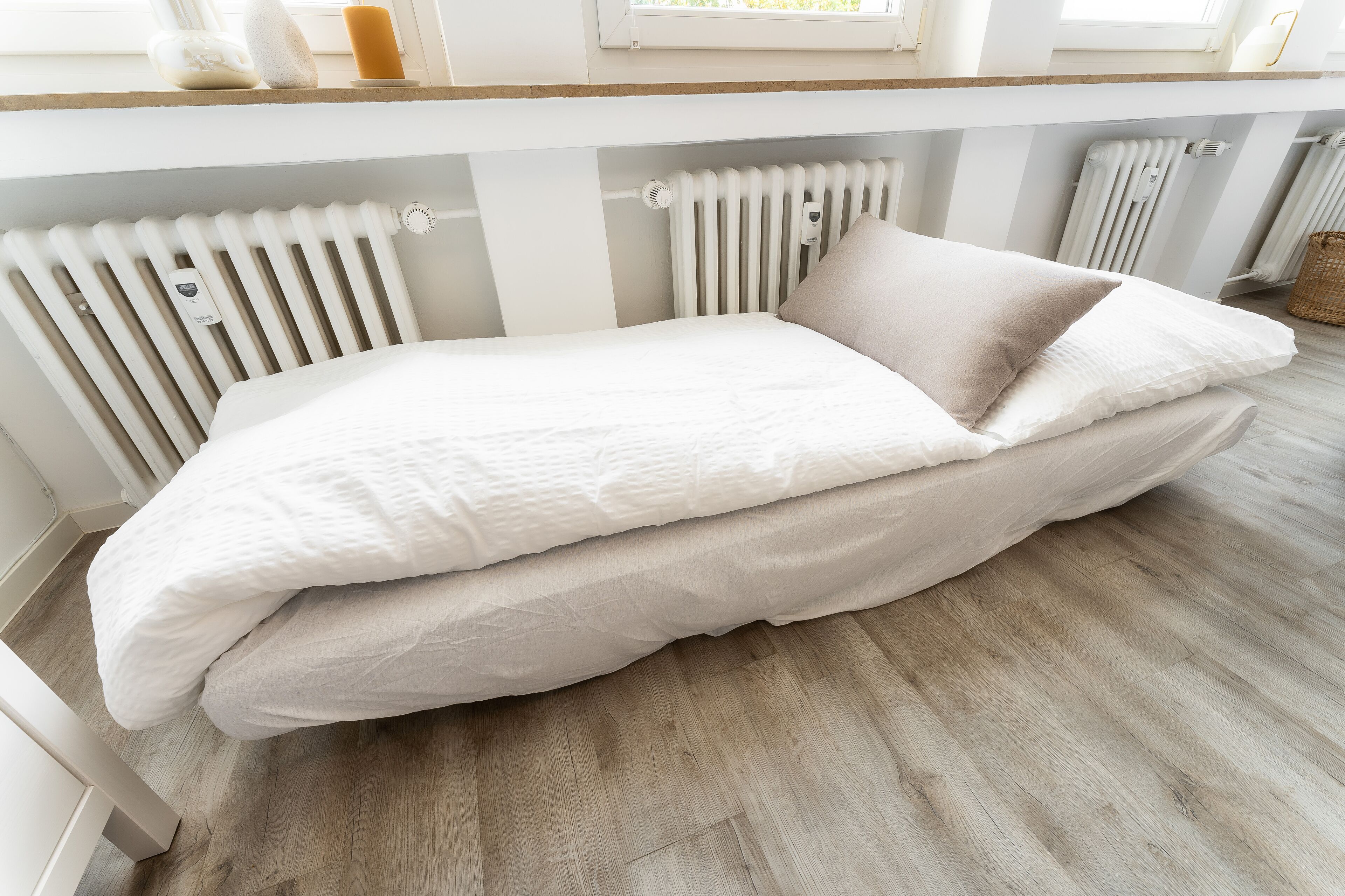 A neatly made bed with a white and beige duvet, positioned under a window with a view of the outdoors.