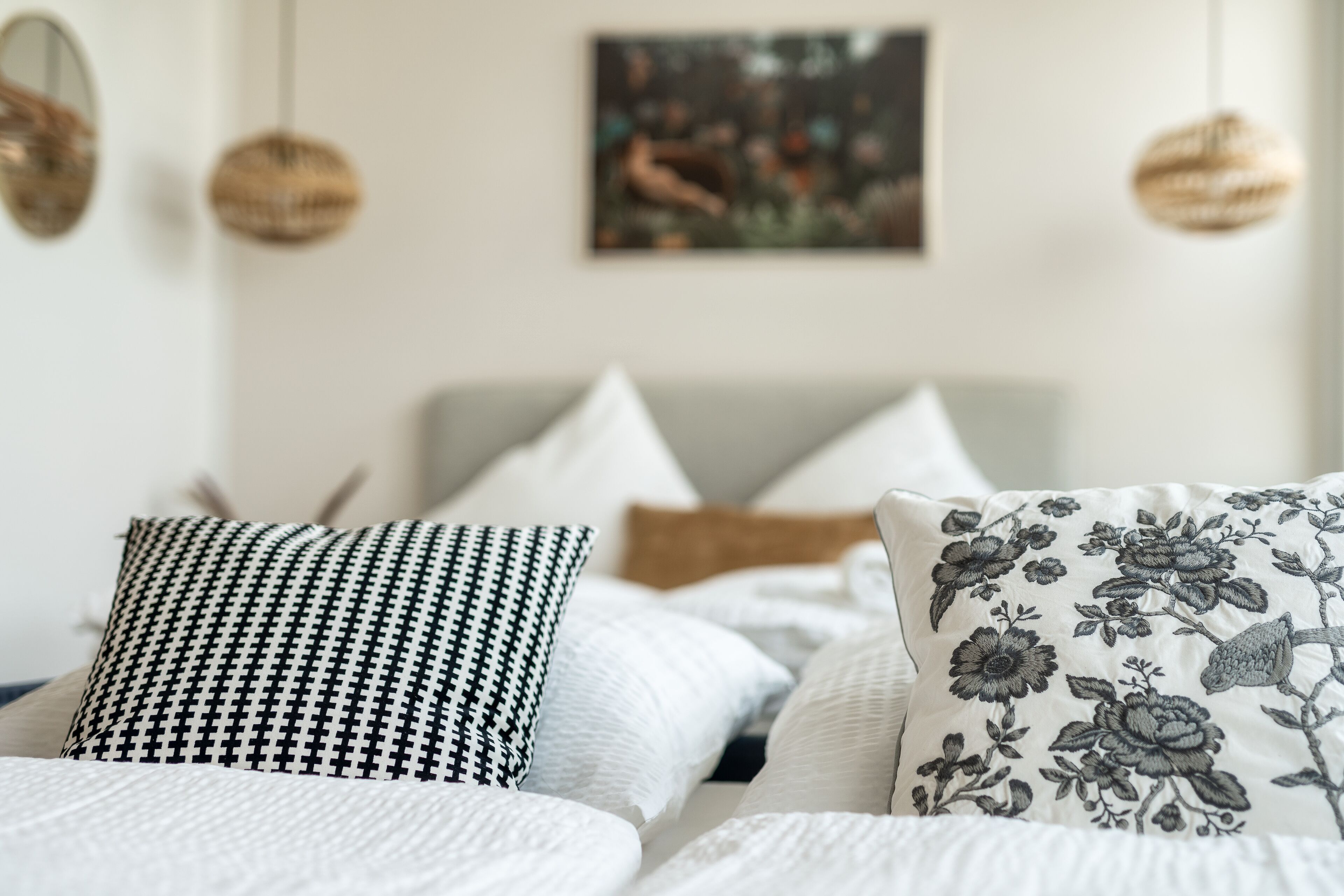 A bed with white bedding and decorative pillows, including a black and white houndstooth and a floral design.