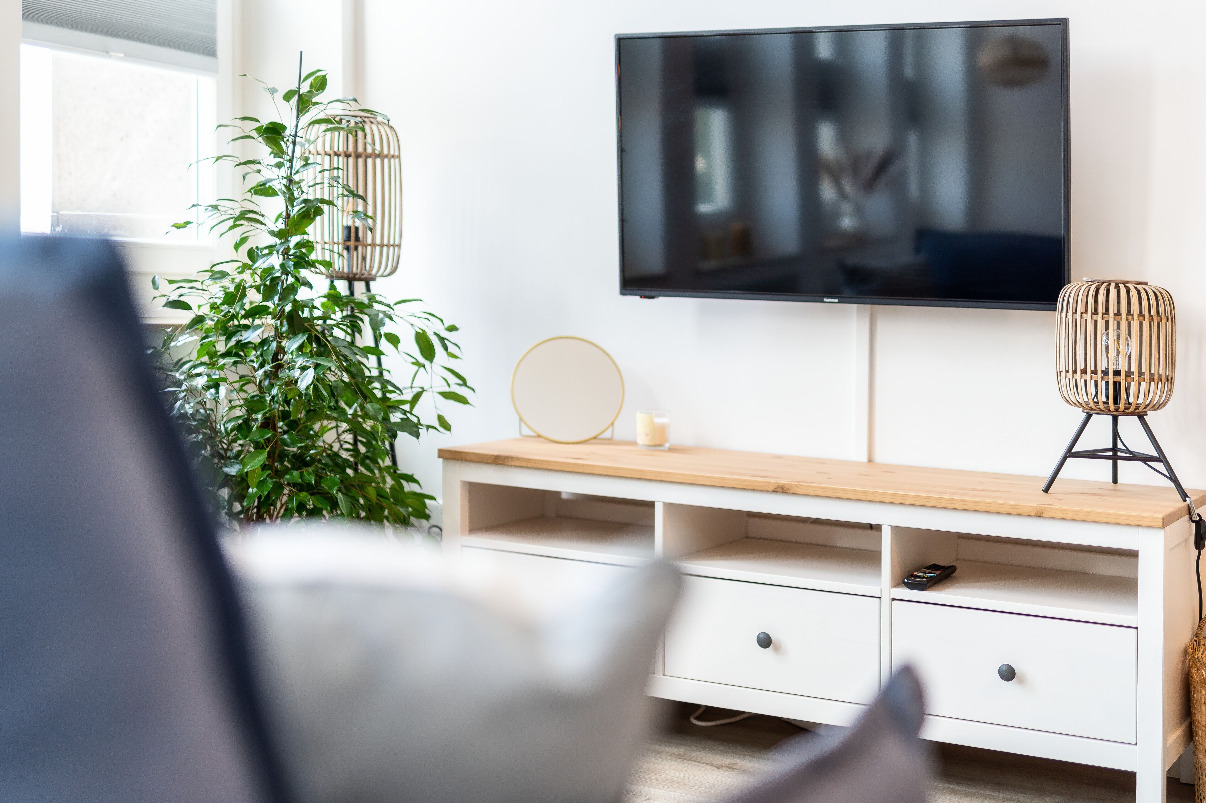 Een moderne woonkamer met een flatscreen televisie aan de muur, een houten console met lades, een bloempot en twee decoratieve lampen.