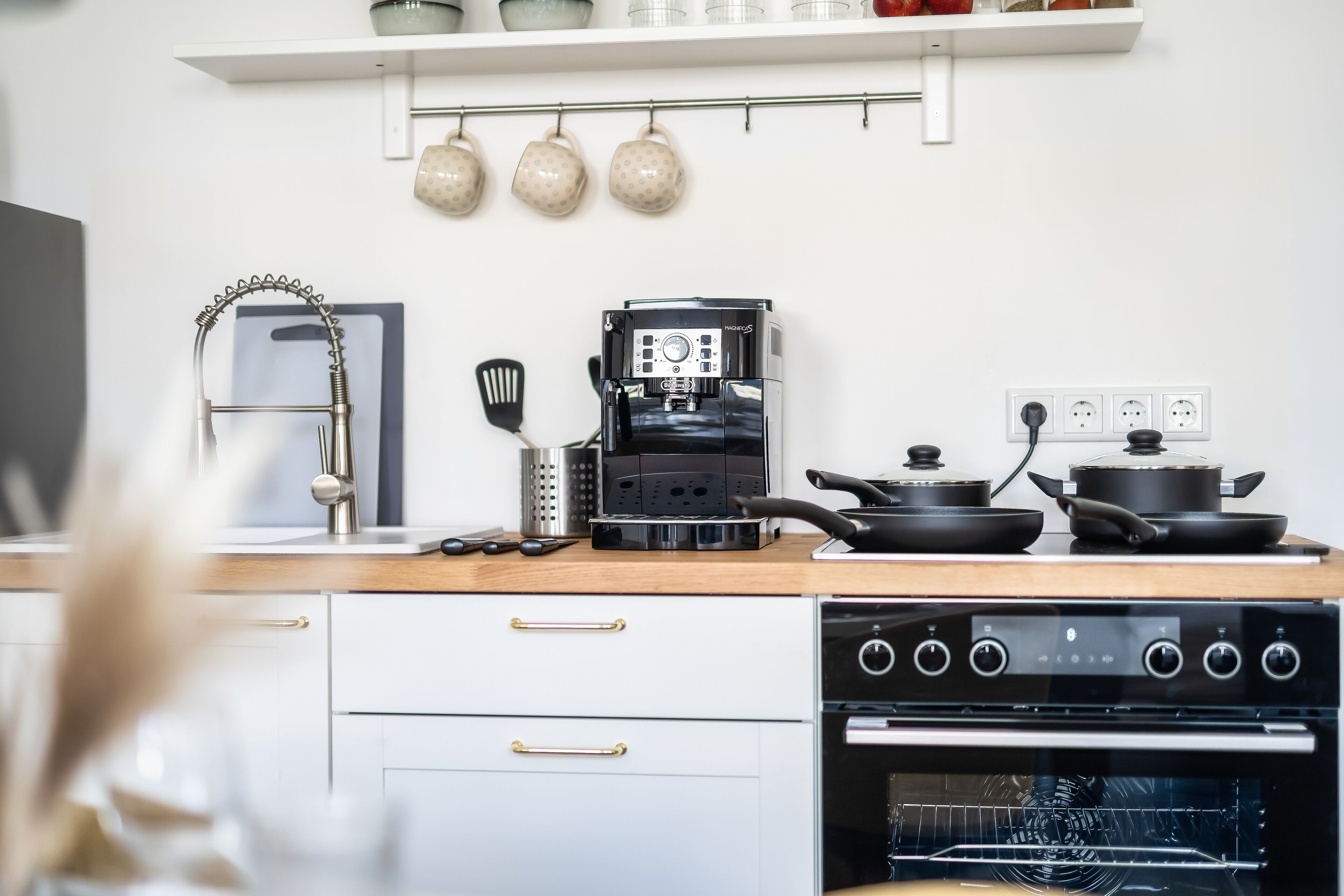 Eine moderne Küche mit Kaffeemaschine, Herd, Backofen und aufgehängten Tassen.