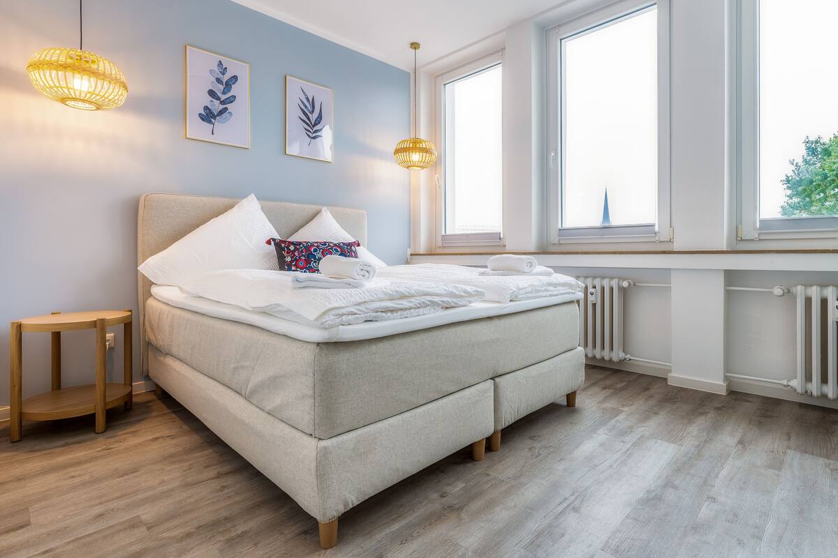 Quarto com cama, mesas de cabeceira, janela e radiador.