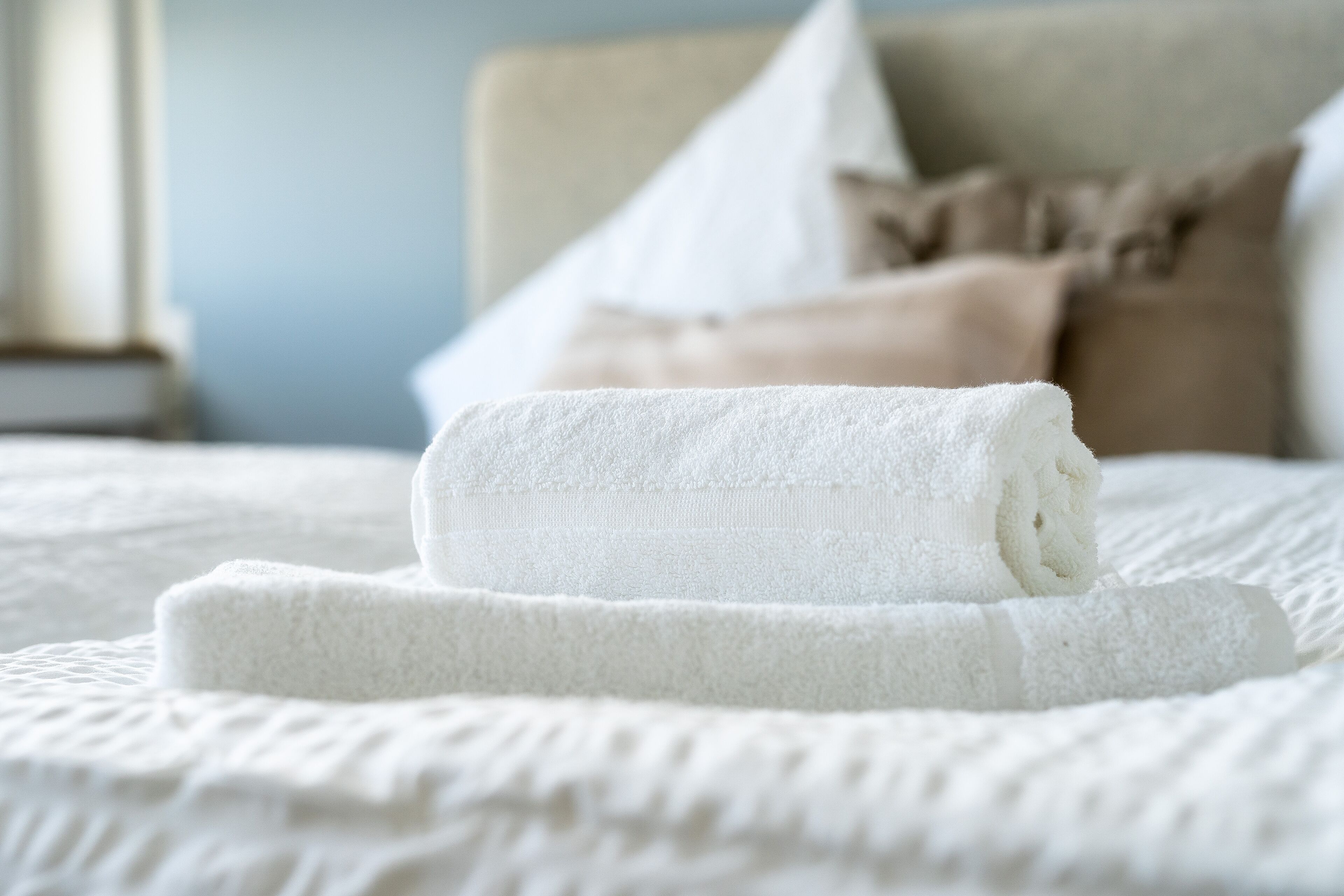 A neatly folded white towel on a bed with a textured white cover.