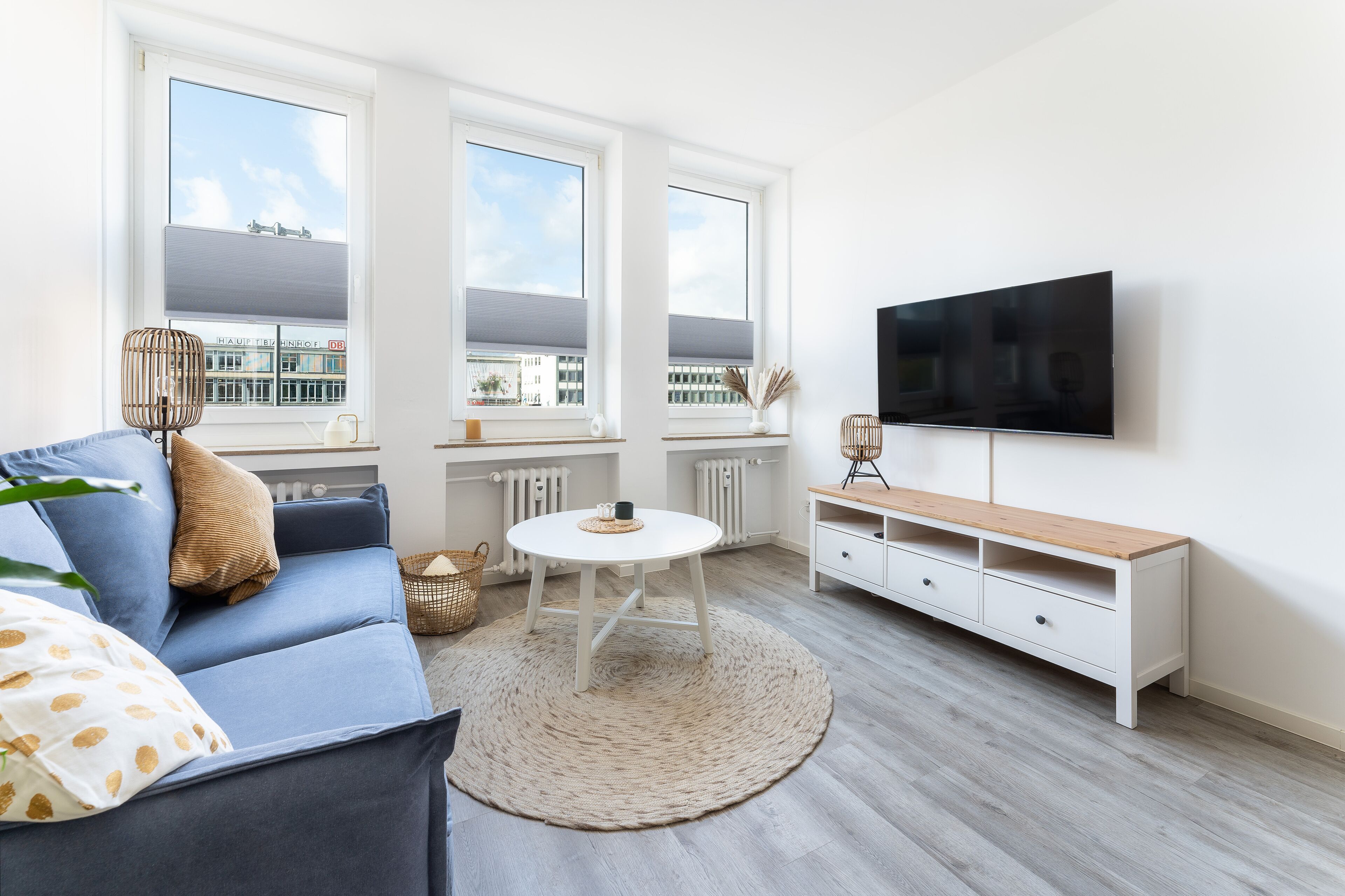 A modern living room with a sofa, a coffee table, a TV, and a view of the city through large windows.