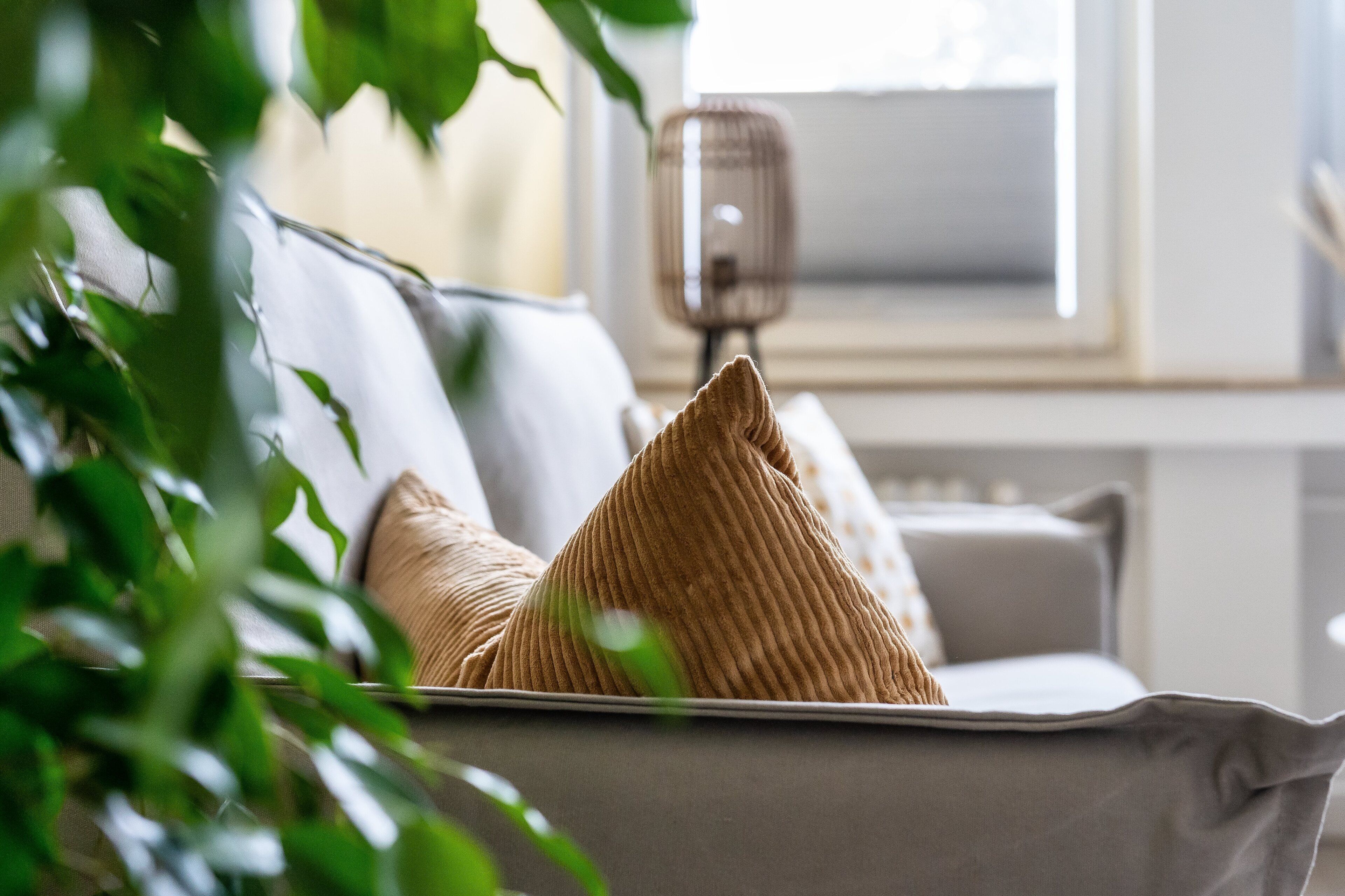 Ein Sofa mit einem gemusterten Kissen, einer Lampe und einem Fenster im Hintergrund.