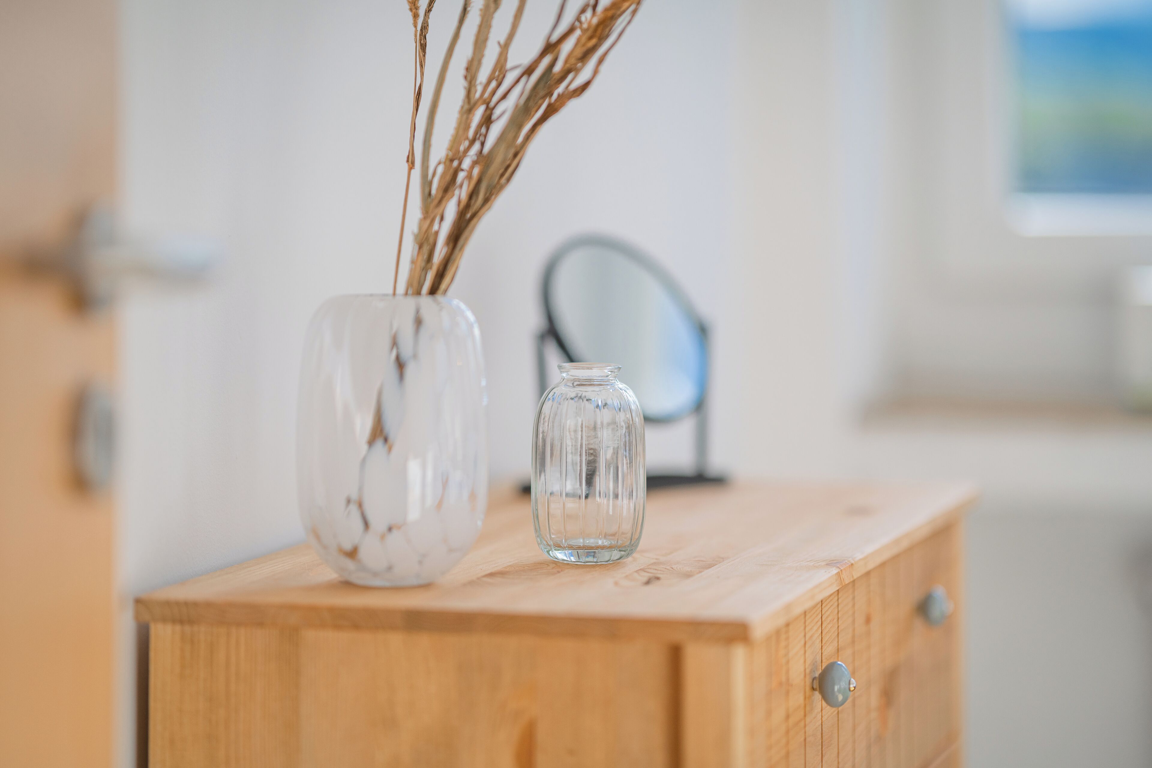 Un meuble en bois contenant deux vases en verre avec des plantes séchées.