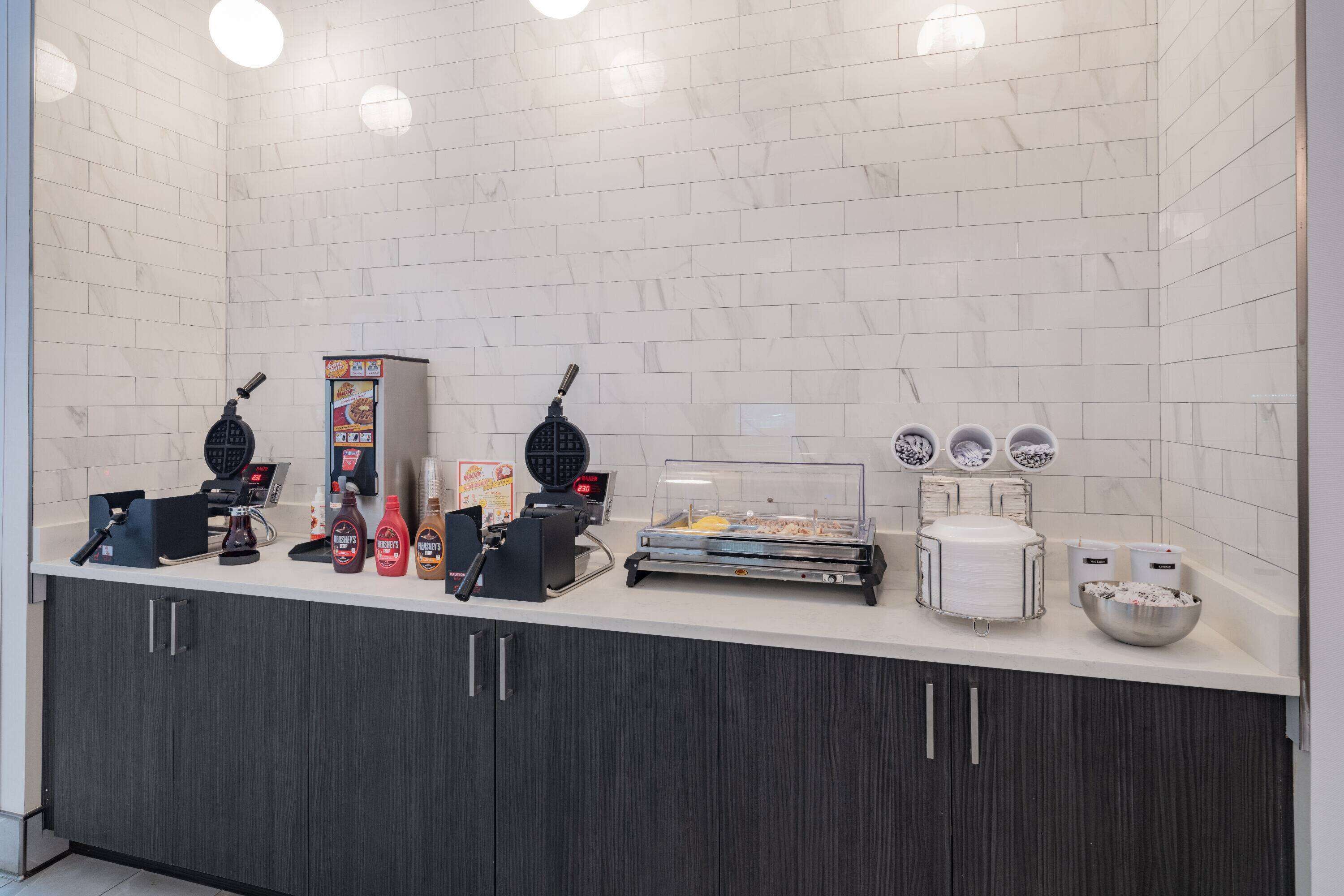Uma estação de pequeno-almoço de serviço, com máquinas de waffles, máquinas de café e dosadores de acompanhamentos.