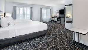 Habitación de hotel con una cama grande, un escritorio, una silla, un televisor y una mesita.