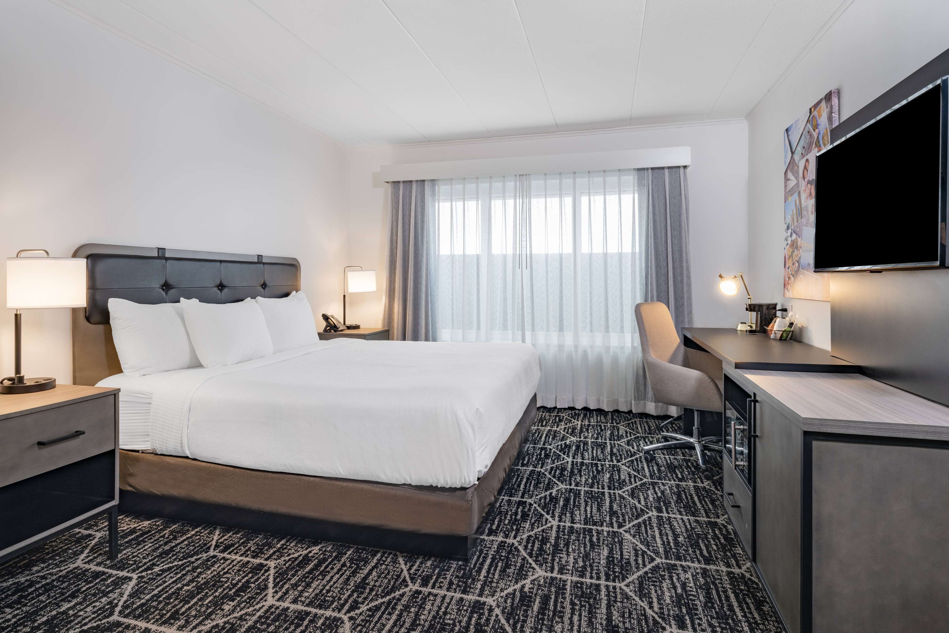 A hotel room with a large bed, a desk, a chair, a TV, and a window with curtains.