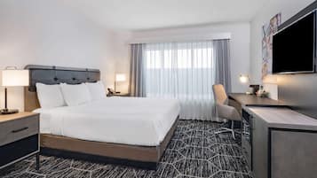 A hotel room with a large bed, a desk, a chair, a TV, and a window with curtains.