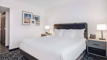 Una camera d'albergo con un letto grande, due comodini con lampade, un piccolo cassetto e un quadro appeso alla parete.
