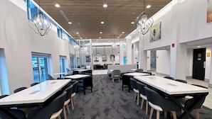 Un salón de conferencias moderno con mesas largas y sillas negras, ventanas amplias y lámparas decorativas.