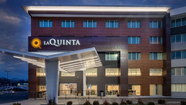 Hotel La Quinta con fachada moderna, entrada cubierta y estacionamiento visible al fondo.