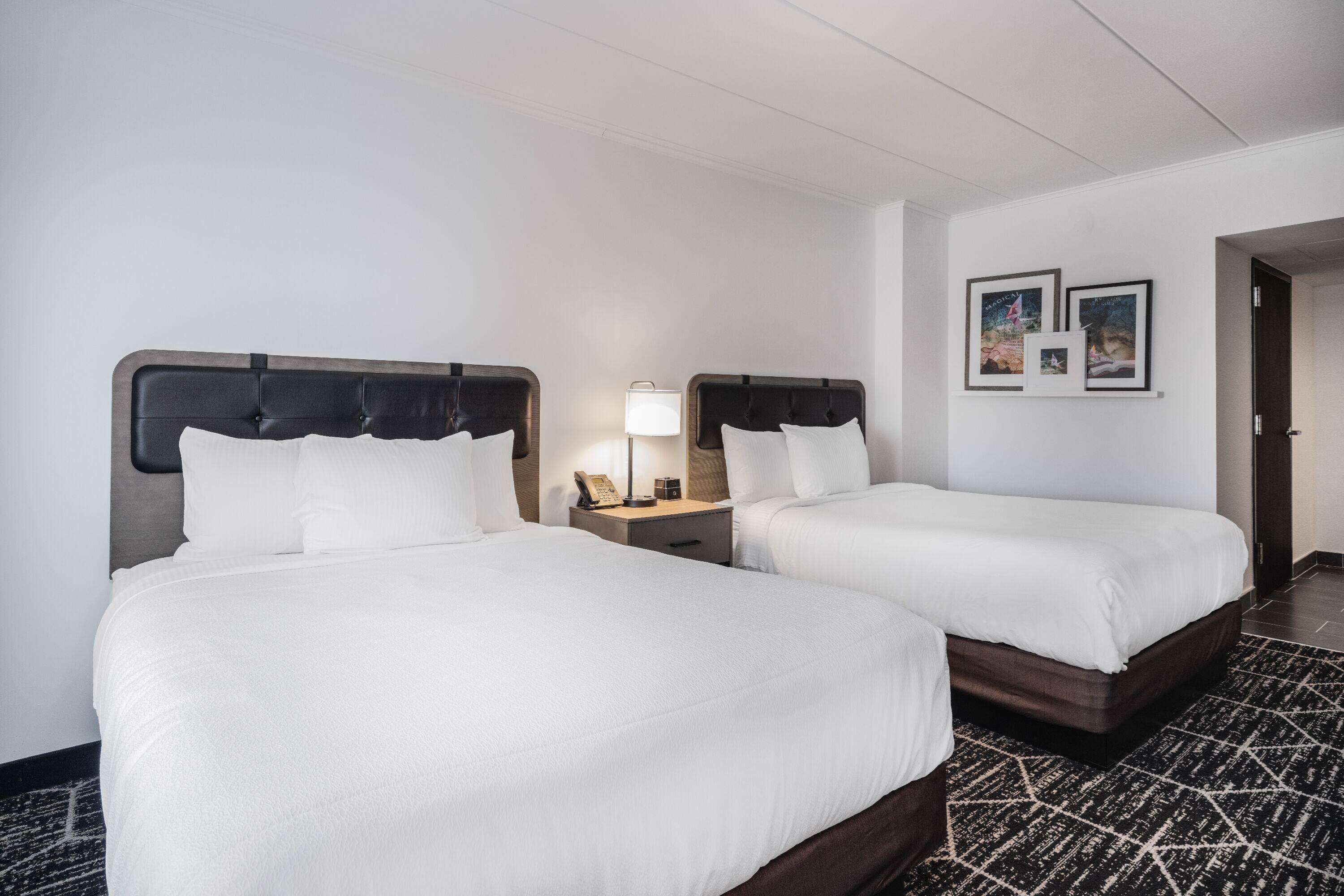 Une chambre d’hôtel avec deux lits, une table de chevet avec une lampe et des tableaux encadrés au mur.