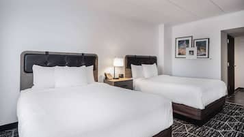 Habitación de hotel con dos camas, una mesita de noche con lámpara y cuadros en la pared.