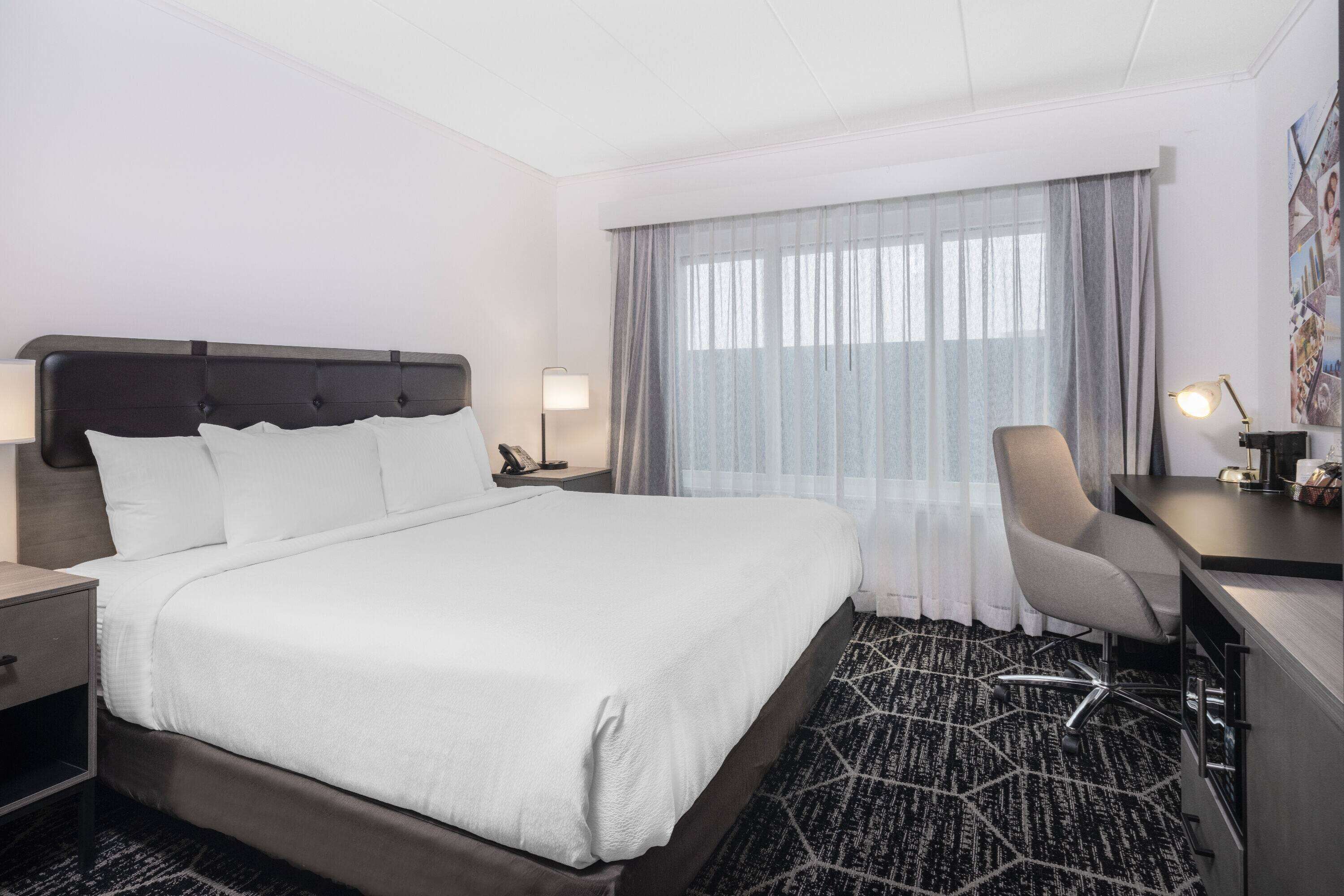 Ein Hotelzimmer mit einem großen Bett, einem Schreibtisch, einem Stuhl und einem Fenster mit Vorhängen.