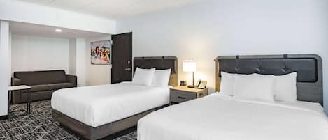 A hotel room with two beds, a sofa, a desk, and a painting on the wall.