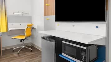 A compact kitchenette with a microwave, a small refrigerator, and a yellow chair.