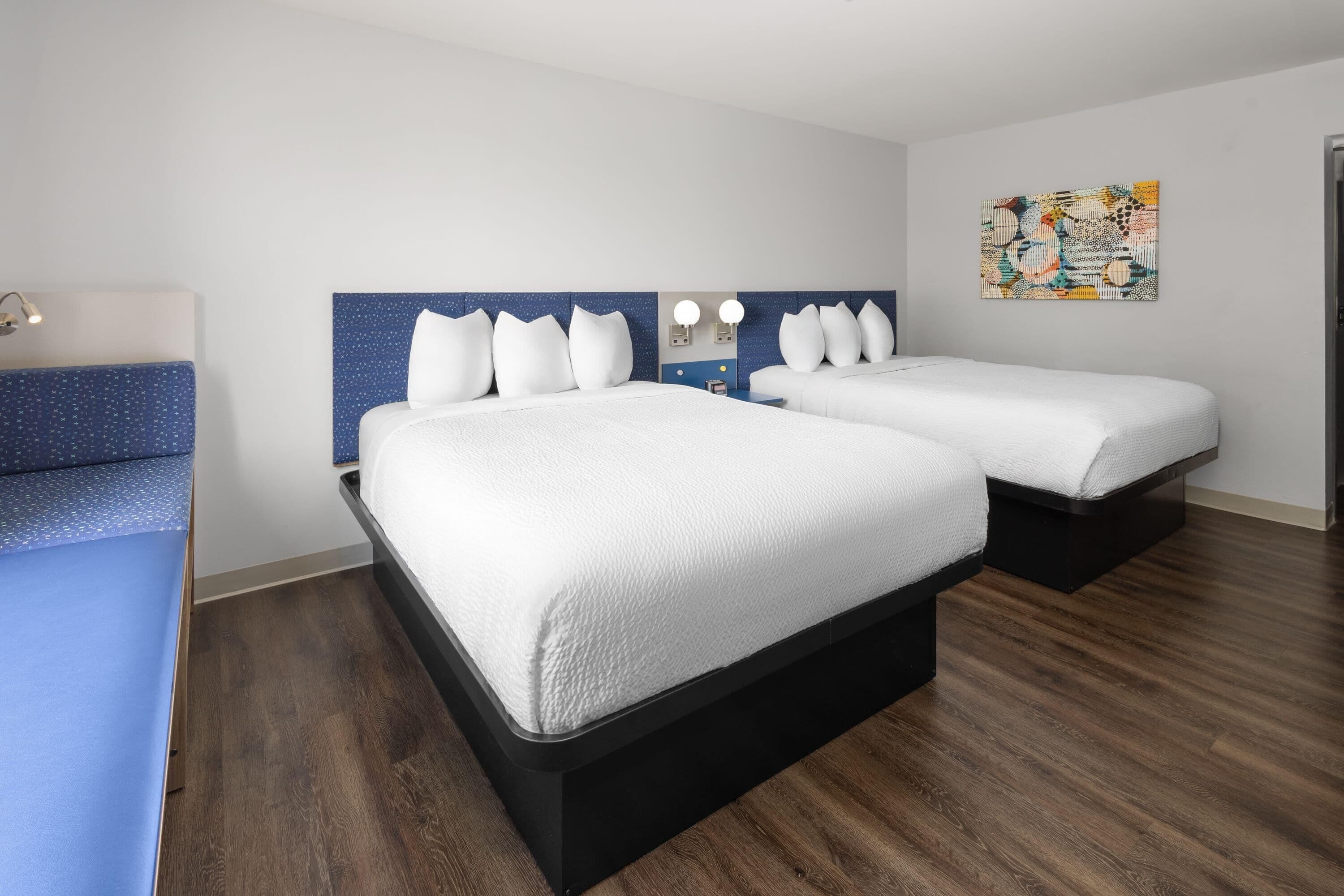 Een hotelkamer met twee bedden, een bureau, een stoel, een spiegel en een kunstwerk aan de muur.