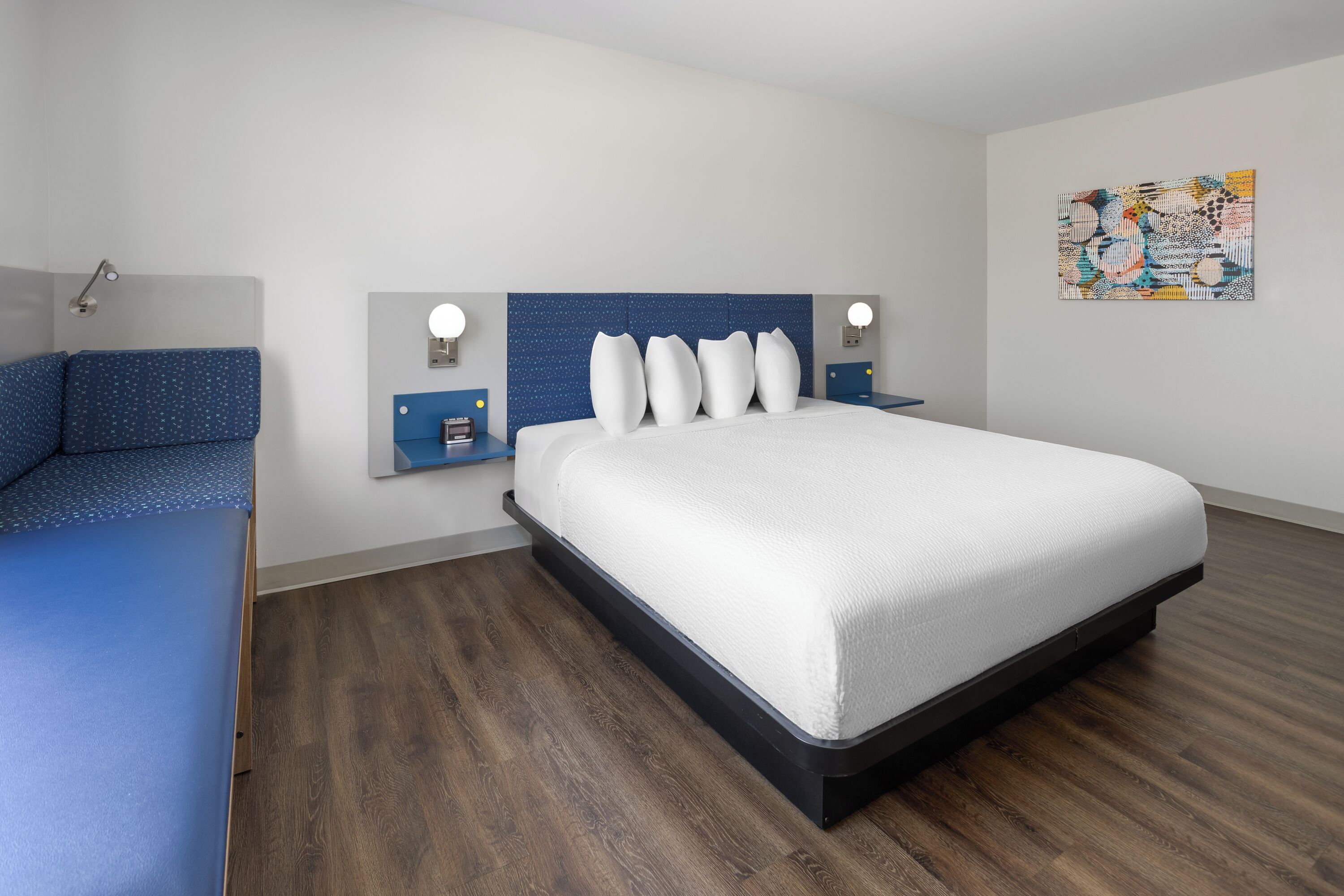 A modern hotel room with a large bed, a bedside table, and a wall-mounted artwork.