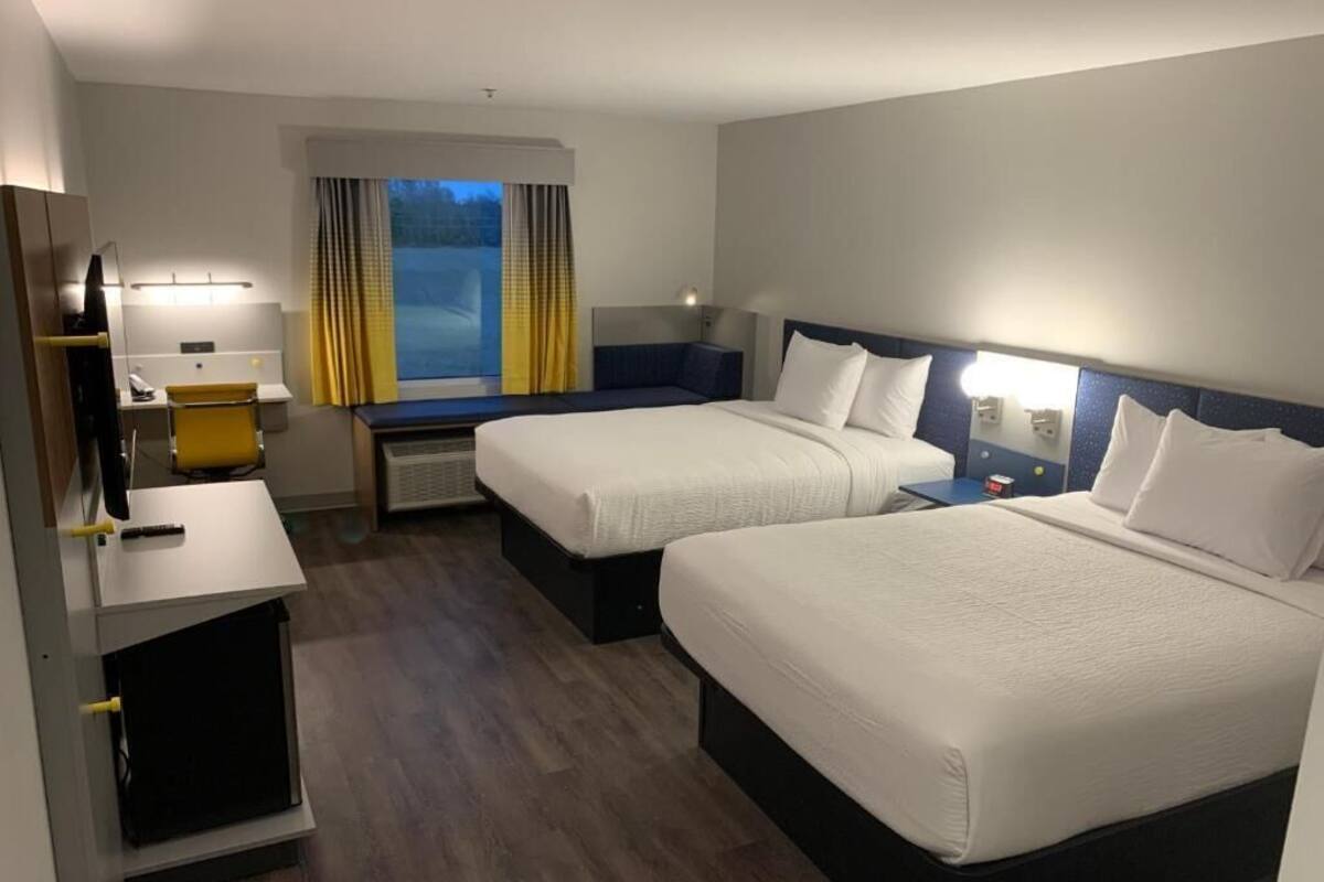 A hotel room with two beds, a desk, a chair, a TV, and a window with curtains.