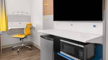 A compact kitchenette with a microwave, a small refrigerator, a yellow chair, and a white countertop.
