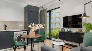 A modern apartment with a kitchen, dining area, and living room. It includes a washing machine, a dining table with chairs, a sofa, a TV, and a large window with a view of buildings. - FortyOnL 610 (Cape Town)