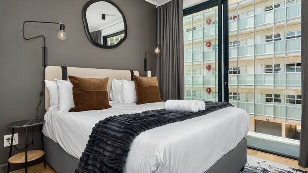 A modern hotel room with a large bed, a round mirror, and a view of a high-rise building. - FortyOnL 610 (Cape Town)
