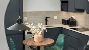 A modern kitchen with dark cabinets, a round table, two green chairs, and a vase with flowers. - FortyOnL 610 (Cape Town)