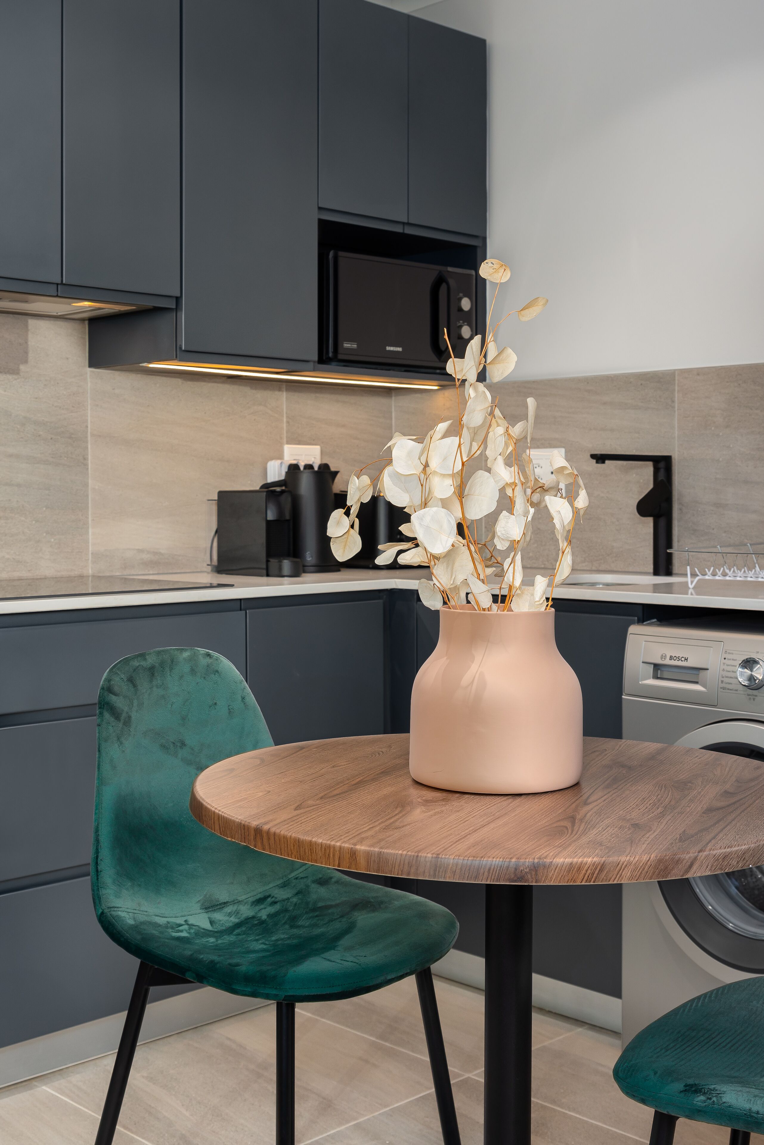 A modern kitchen with dark cabinets, a round wooden table, and a green chair.