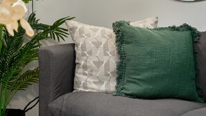 A modern living room with a gray sofa, a green throw pillow, a white patterned pillow, and a round mirror on the wall. - FortyOnL 610 (Cape Town)
