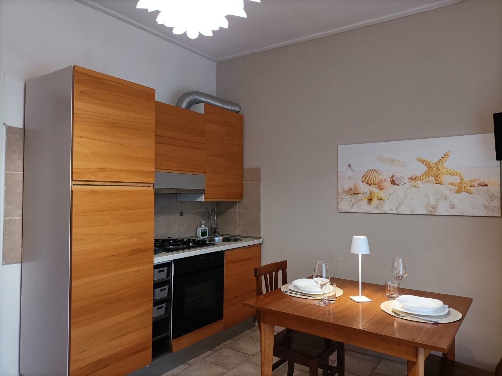 Cozinha compacta com armários de madeira, fogão a gás e mesa de jantar posta para dois.