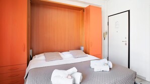 A hotel room with a bed, a wooden wardrobe, a door, and a white wall. - Studio apartment "Holiday Sea" with Terrace & A/C (Diano Marina)