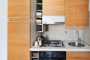 Una cocina con armarios de madera, un lavamanos de acero inoxidable, una estufa a gas y un horno empotrado.