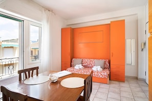 Una habitación con una mesa de comedor de madera, un sofá con cojines estampados y una puerta corrediza naranja.