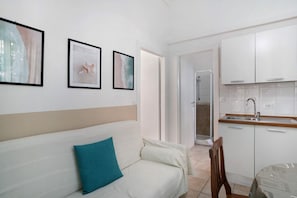 Une cuisine moderne avec des meubles blancs, un évier et une douche visible à travers une porte ouverte.