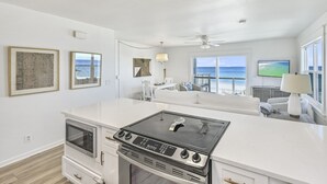 A kitchen with a stove, oven, and microwave. There are framed pictures on the wall and a view of the ocean through large windows. - Beach Front with Balcony and Grill (Panama City Beach)