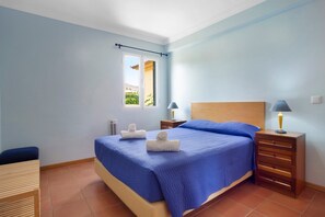 A bedroom with a bed, two bedside tables, a window, and a chair.