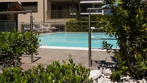 Une piscine entourée de chaises longues, de verdure et d’un bâtiment doté de balcons.