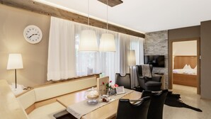 Une chambre d’hôtel moderne avec un plafond en bois, un coin repas comprenant une table et des chaises, un canapé, un téléviseur et un lit avec une tête de lit en bois.