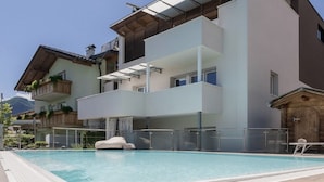 Un edificio moderno de varios pisos con piscina, balcones y un paisaje montañoso de fondo.